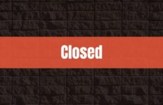 Text that says Closed on a red rectangle with a brick wall in the background.
