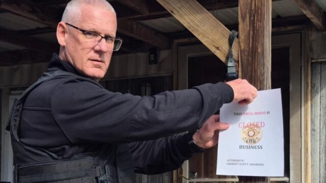 Franklin Co. Sheriff Scott Andrews hangs a "This Drug House Is Closed" sign on a house following a drug raid in which a Hall Co. man was arrested.  (Franklin Co. Sheriff's Office photo)